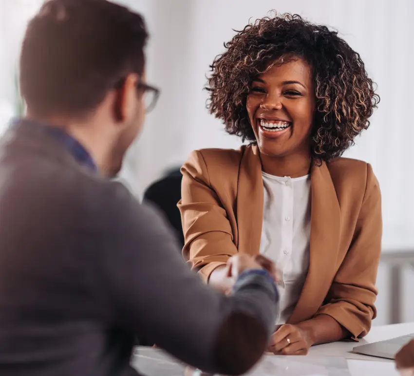 Two professionals shaking hands during an interview or meeting in an office setting.