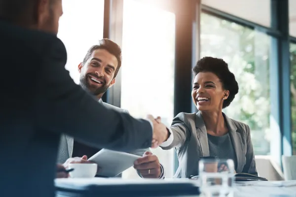 Smiling colleagues in a meeting, shaking hands.