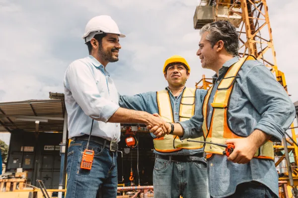 A construction site manager shakes hands with a contractor in front of a crane.